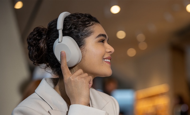 Woman wearing WH-1000XM5 headphones in street, touching earcup to activate touch control settings