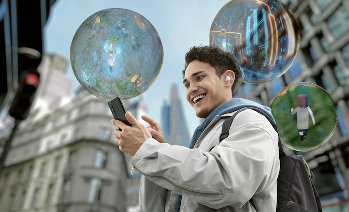 A man with a backpack stands on a city street while smiling at his phone. Three bubbles with  video game scenes inside are floating around him.