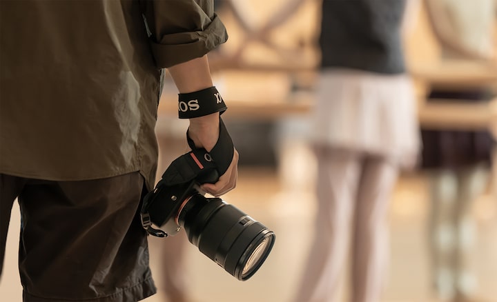 Usage image showing a man carrying in one hand, apparently effortlessly, a camera body with the lens mounted and wrist strap attached