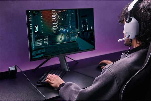 Man wearing INZONE H9 headset playing games on a monitor with game screen shot showing nighttime city scene