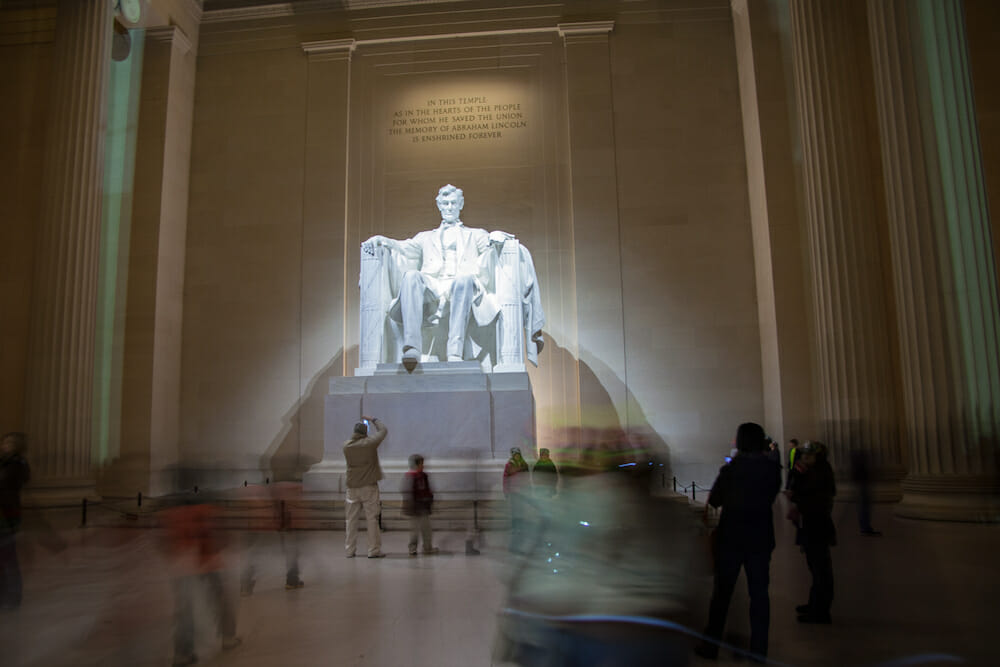 Adults and kids in motion blur in front of the statue within the Lincoln Memorial. 