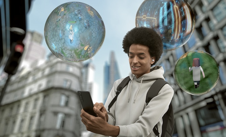 A man with a backpack stands on a city street while smiling at his phone. Three bubbles with  video game scenes inside are floating around him.