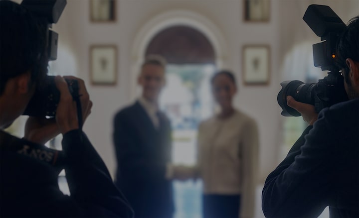 Photographers standing in front of a man and a woman shaking hands, capturing the moment.