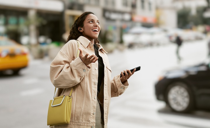 Woman wearing LinkBuds S while walking in a town and talking on her smartphone