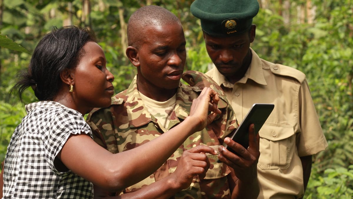 Three dark-skinned people are looking at a phone together outside