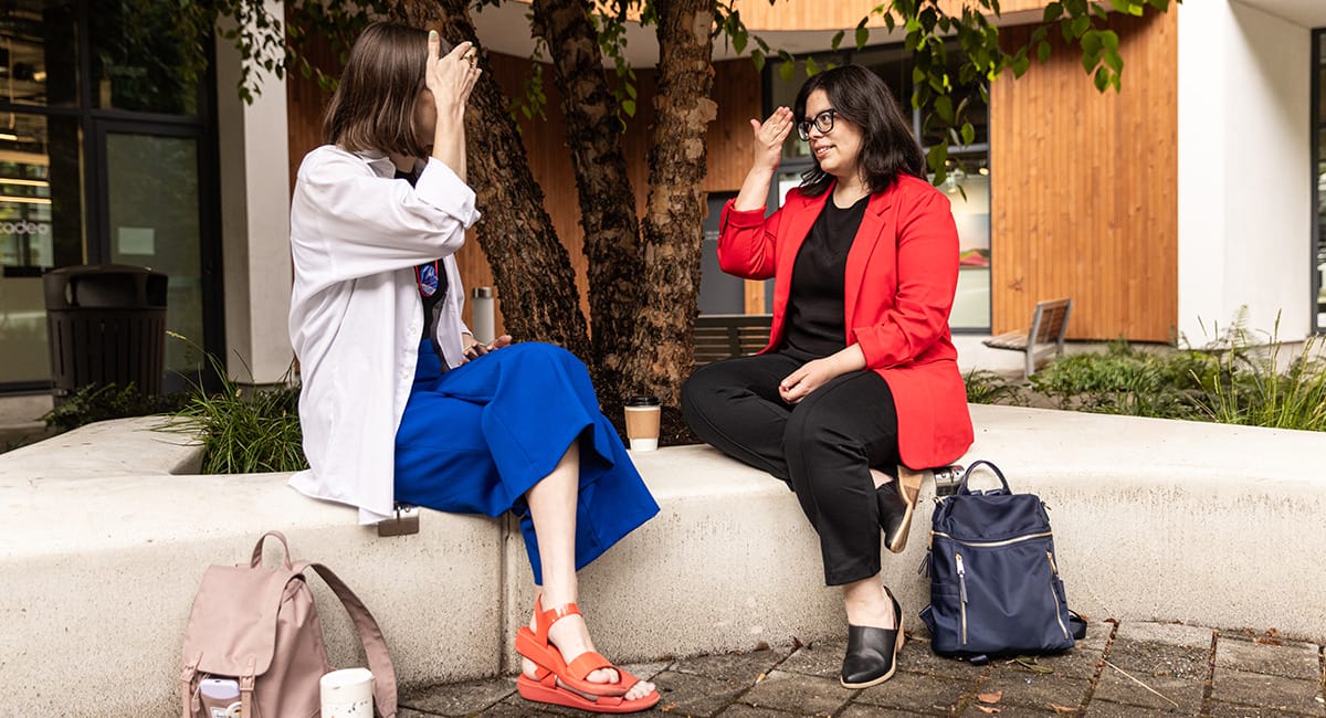  Two women facing each other on a curved white bench while they practice American Sign Language. Text says: Deaf-friendly curved seating makes signing easier, and points to the bench. A label "Sensory retreat space" points to a lone bench in the background. And it says "BONUS: Sturdy, fat-friendly benches" as well.