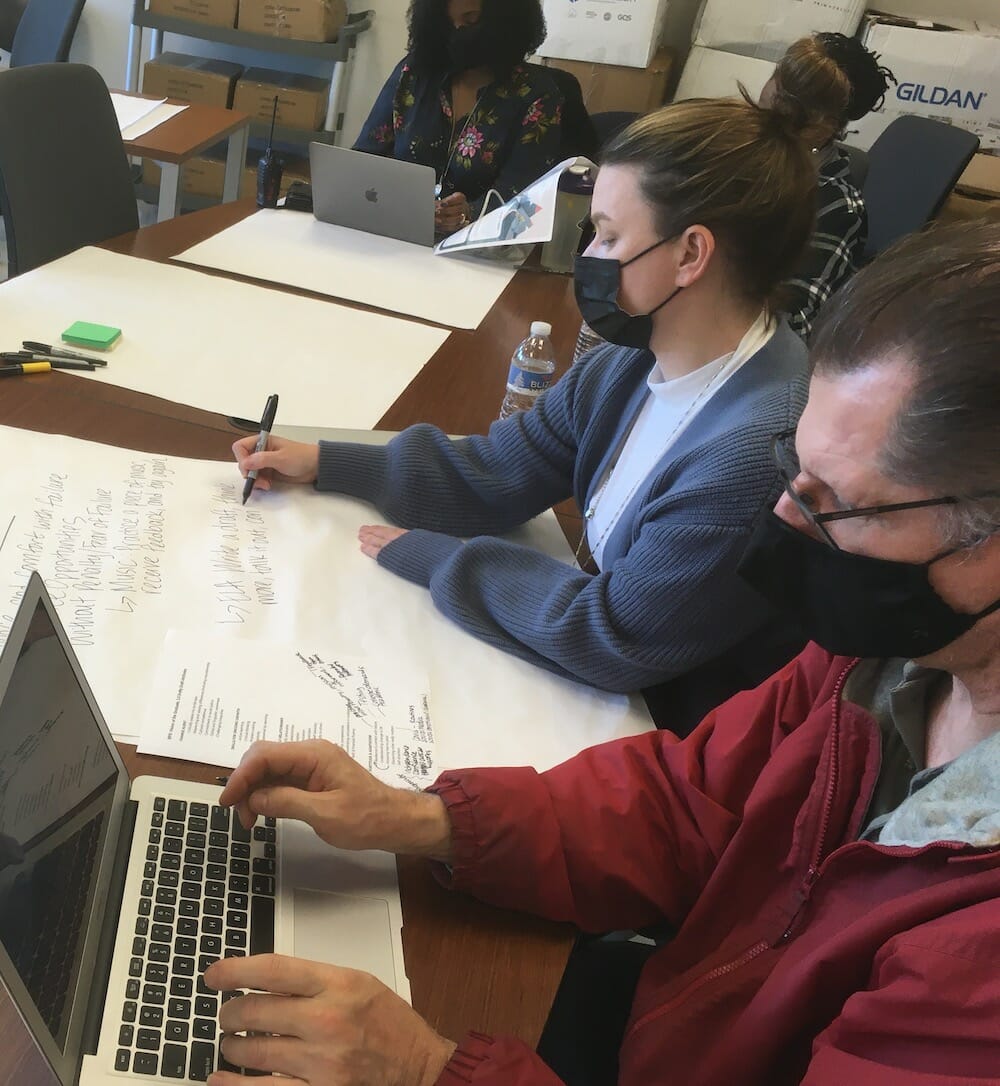 Adults seated working on laptops and paper