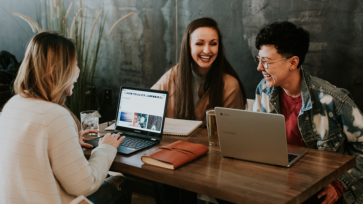 Three people talking and smiling around their computers